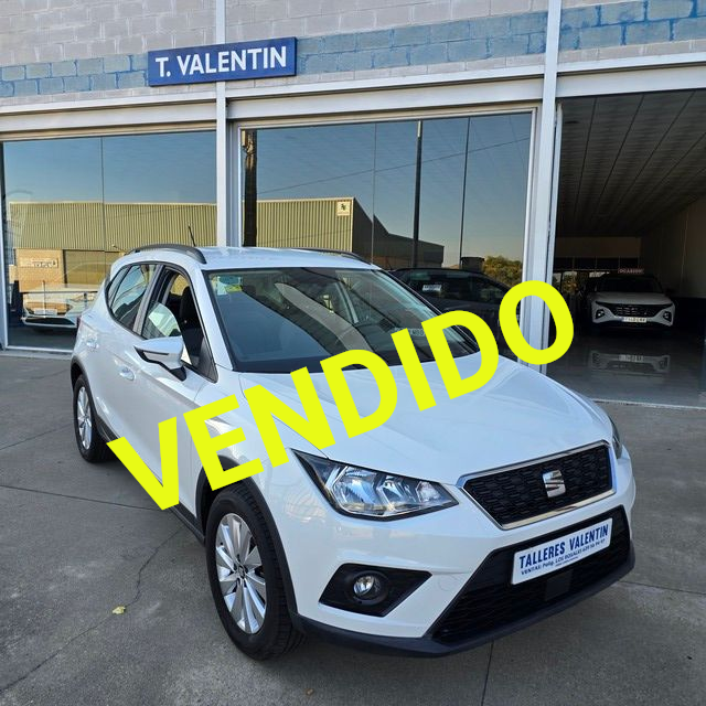 Un coche plateado está aparcado delante de un concesionario de automóviles.