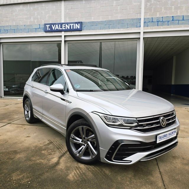 Un coche plateado está aparcado delante de un concesionario de automóviles.