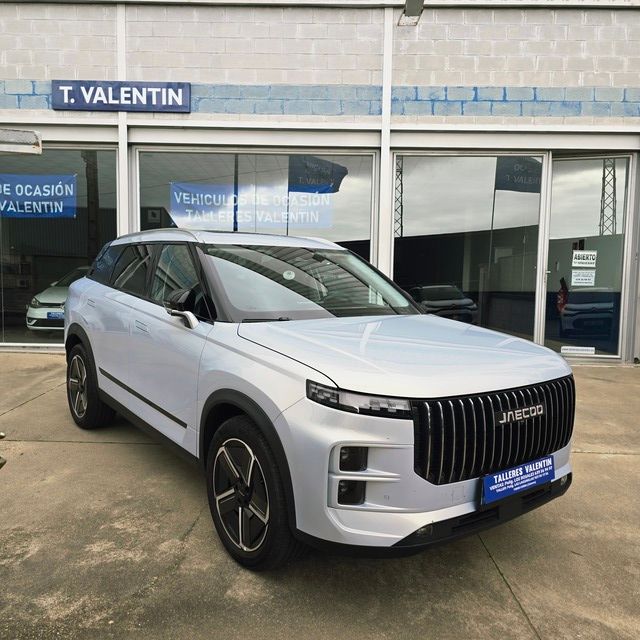 Un coche rojo está aparcado delante de un concesionario de automóviles.