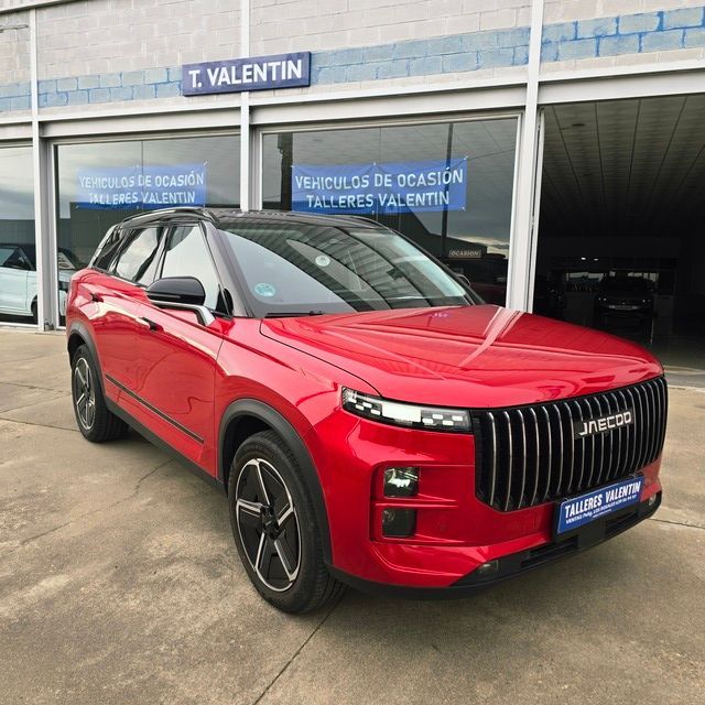 Un Nissan Juke rojo está estacionado frente a un concesionario de automóviles.