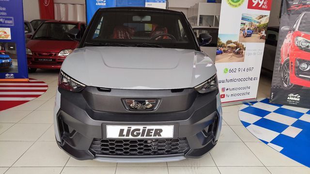 Un coche plateado está aparcado delante de un concesionario de automóviles.