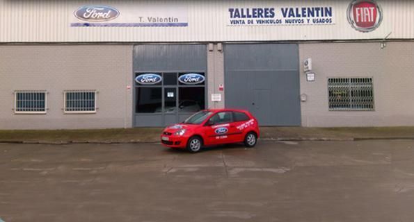 Un coche rojo está aparcado delante de Talleres Valentín.