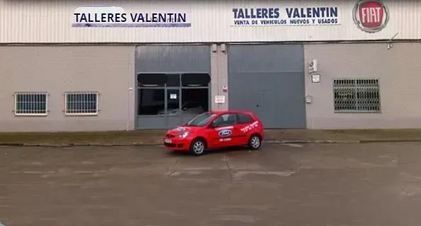 Un coche rojo está aparcado delante de Talleres Valentín.