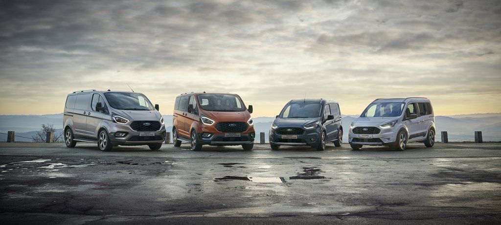 Un grupo de furgonetas Ford están estacionadas una al lado de la otra en una carretera mojada.