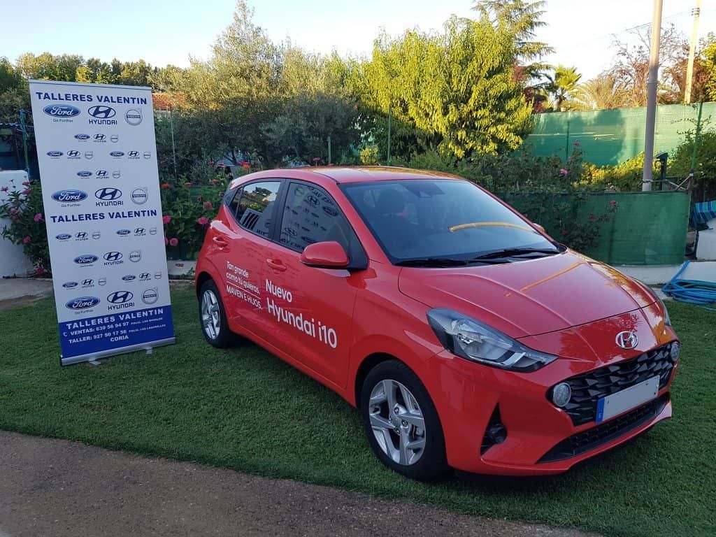 Un coche rojo está estacionado delante de un cartel que dice Hyundai.