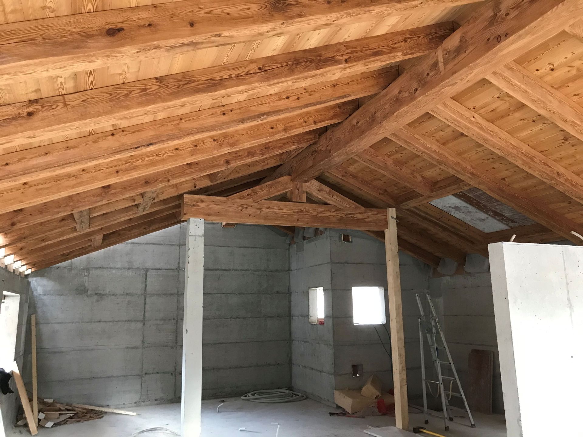 Intérieur d'un bâtiment en construction. Charpente apparente en bois au-dessus de murs en béton.