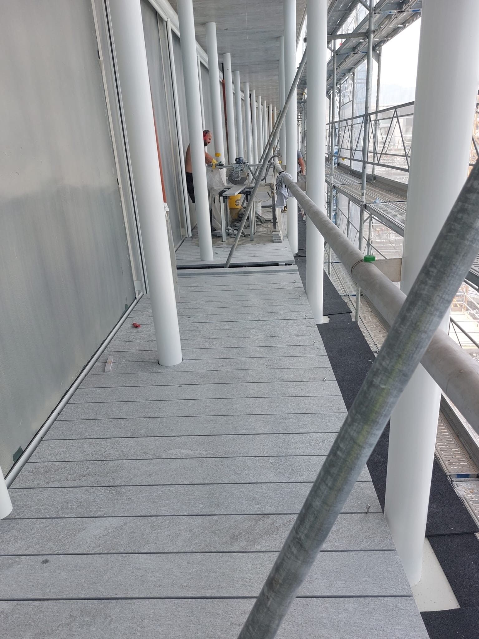 Des ouvriers travaillent sur des échafaudages, un sol gris et une rambarde métallique.