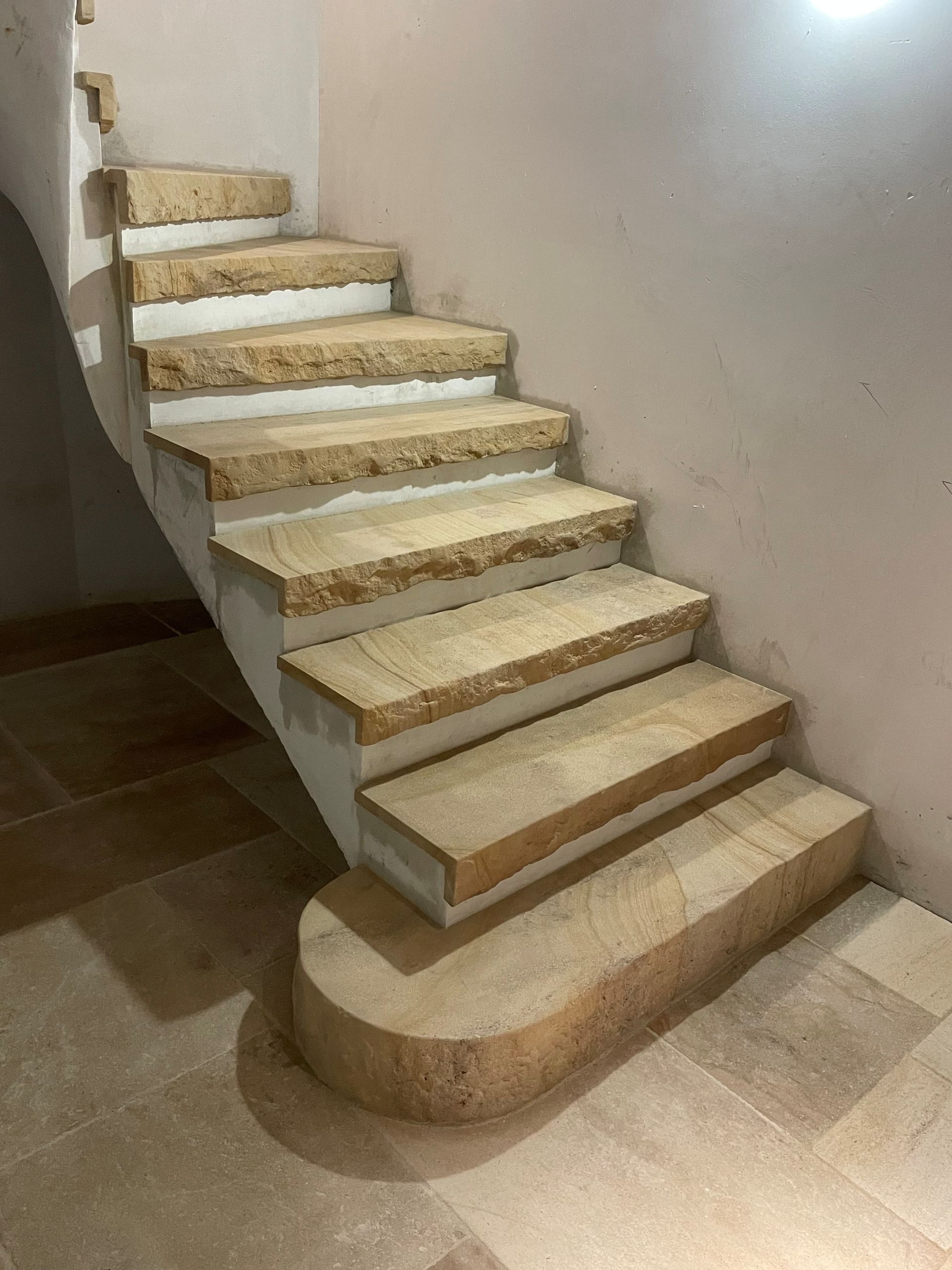 Escalier en pierre aux marches beiges et aux supports blancs, adossé à un mur rose pâle.