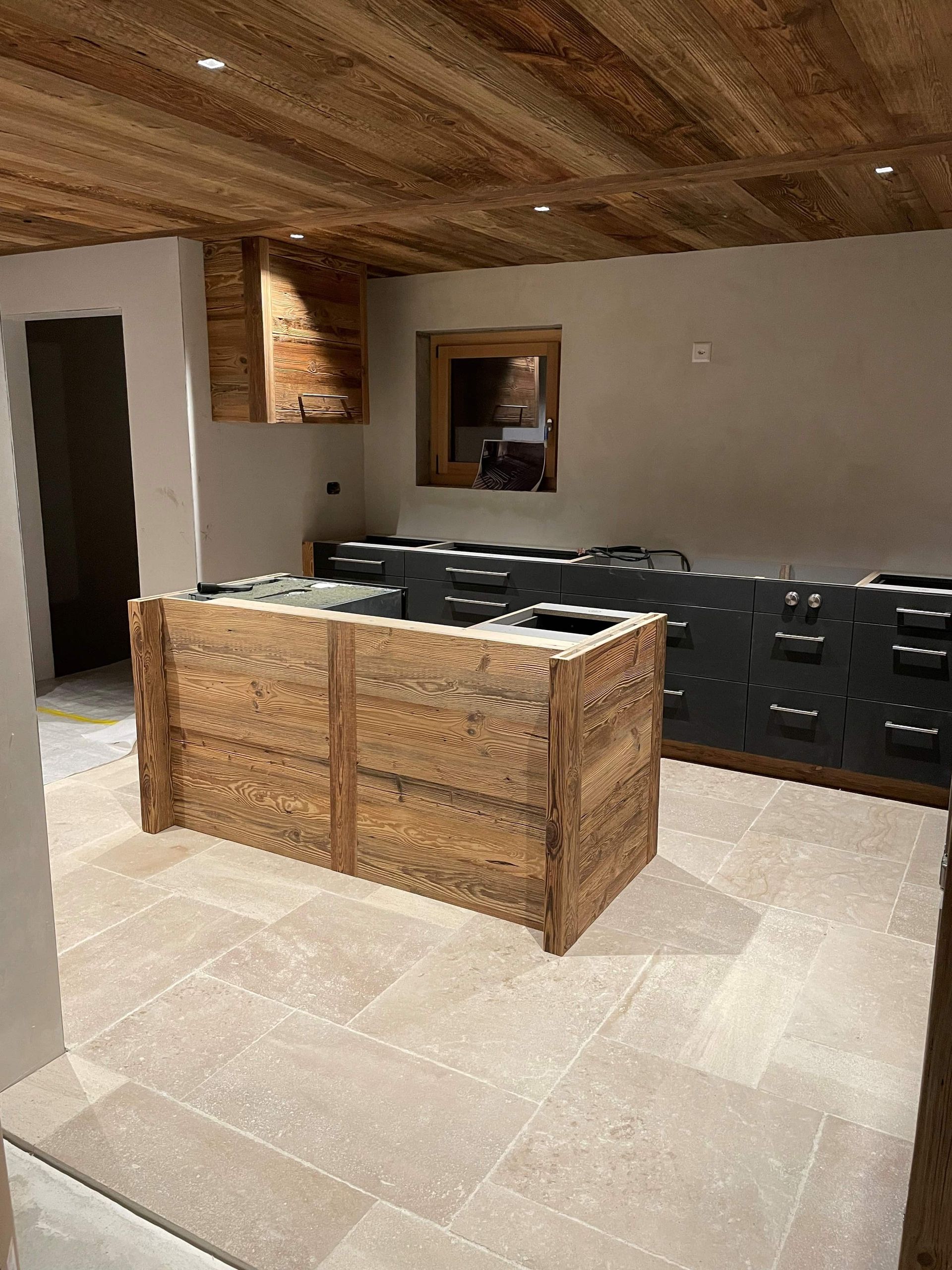 cuisine en cours de construction avec sol en carrelage, ilot et plafond en bois.