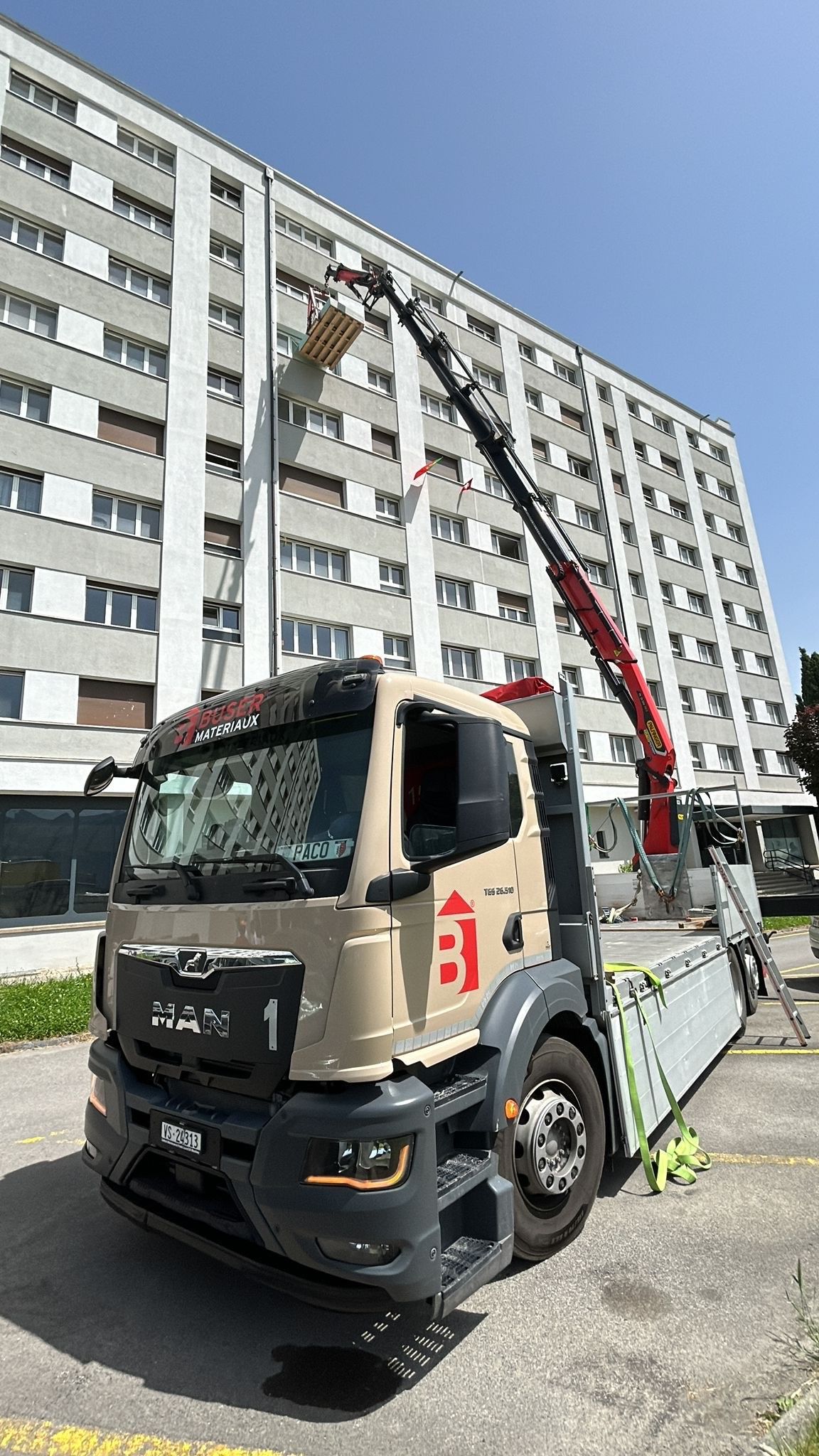 un camion grue de Buser Matériaux en action devant un immeuble