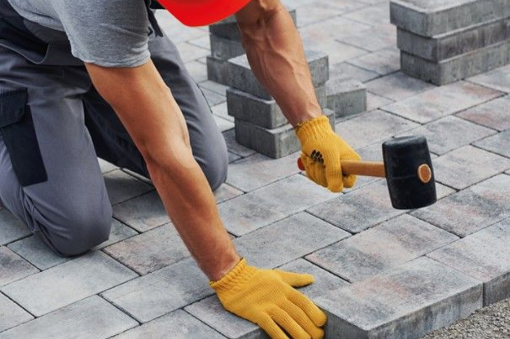 un homme en train de poser des pavés avec un maillet et des gants jaunes