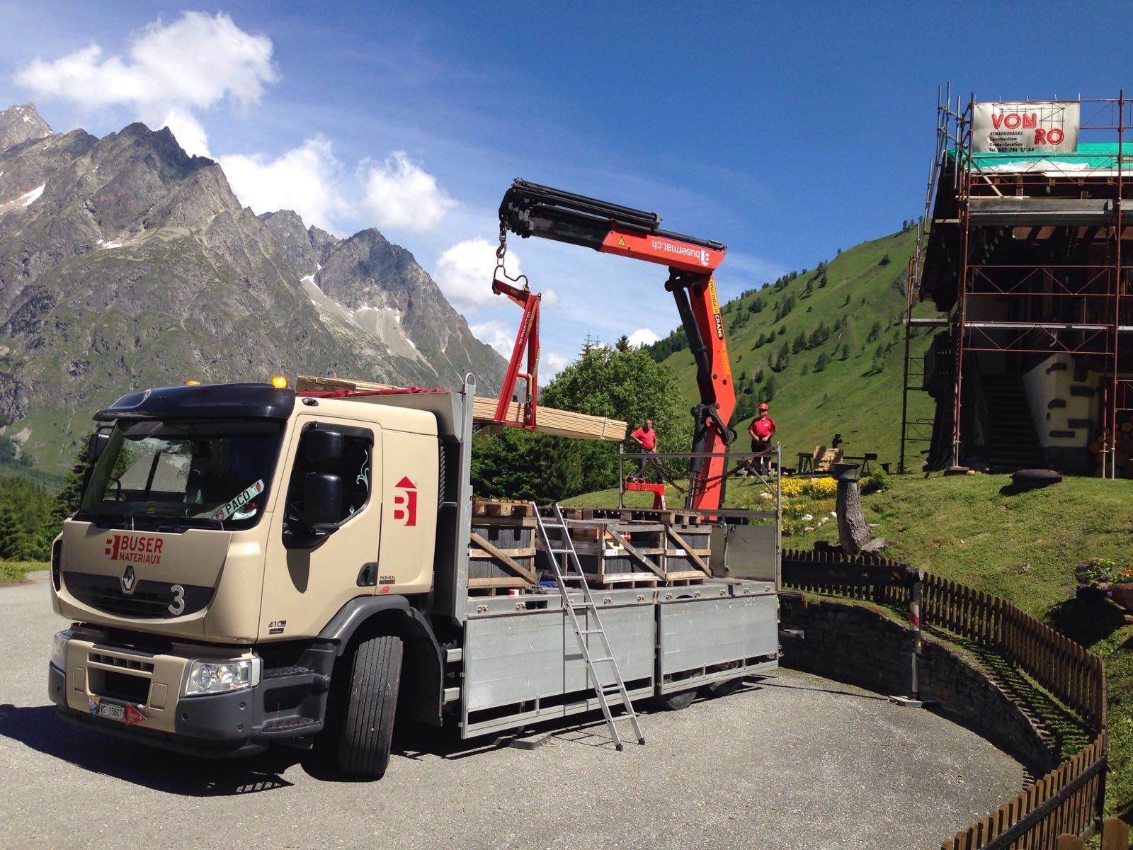 un camion grue de Buser Matériaux avec des montagnes au fond transportant du bois