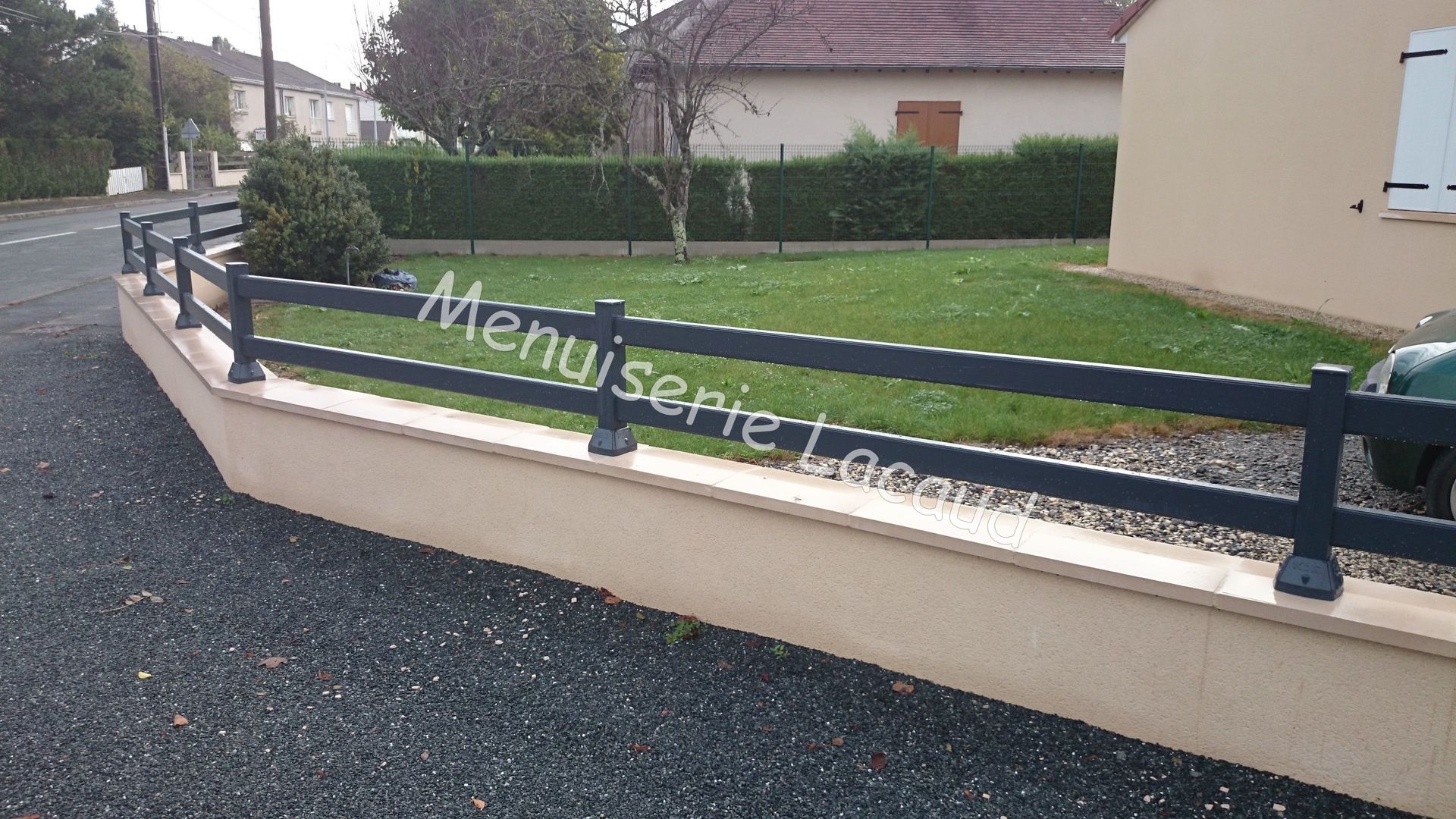Un mur incurvé couleur crème avec une balustrade bleu foncé et une cour gazonnée jouxtant une maison par temps de pluie