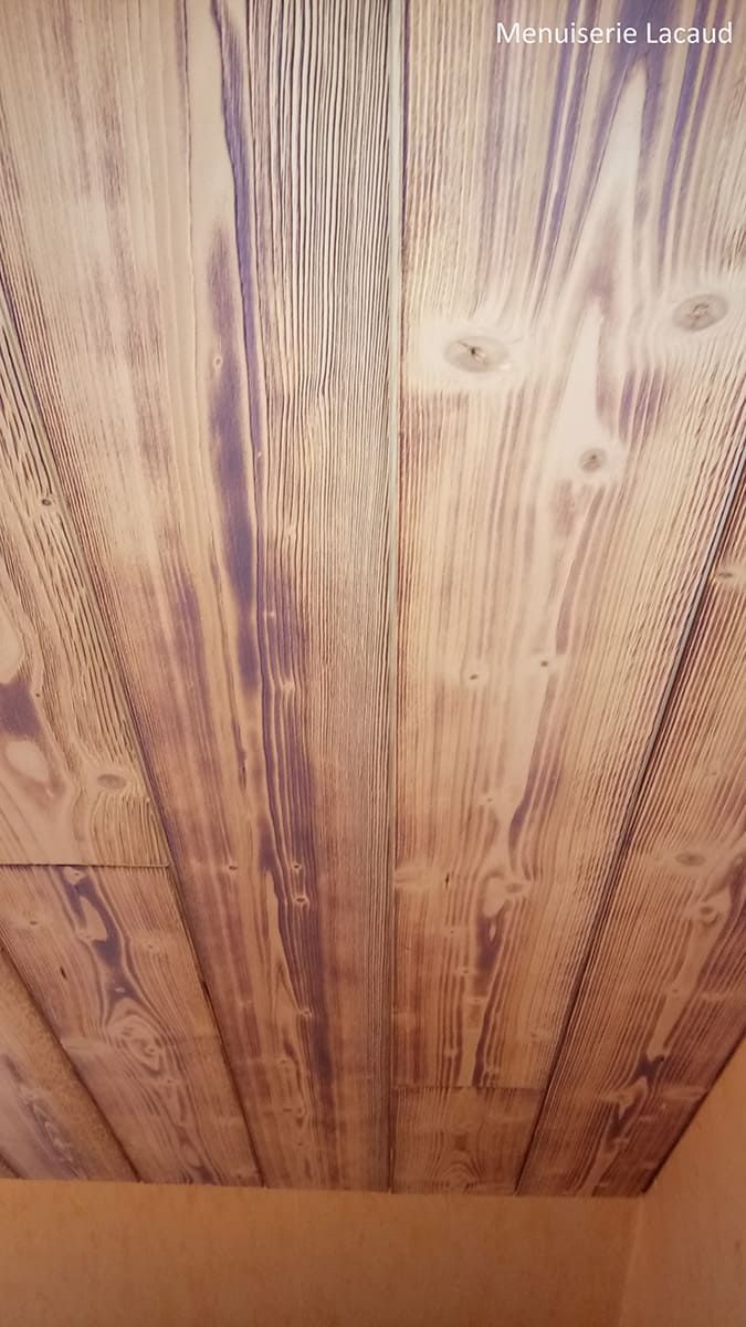 Gros plan sur des planches de plafond en bois patiné, laissant apparaître le grain et les nœuds.