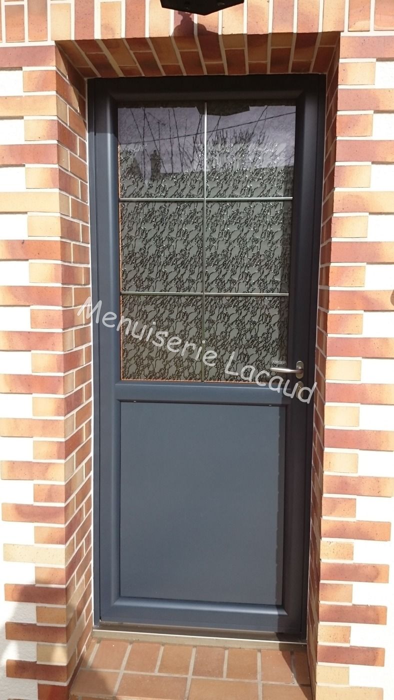 Porte noire étroite avec fenêtre en verre dépoli, encastrée dans un mur de briques avec un cadre en briques arqué.