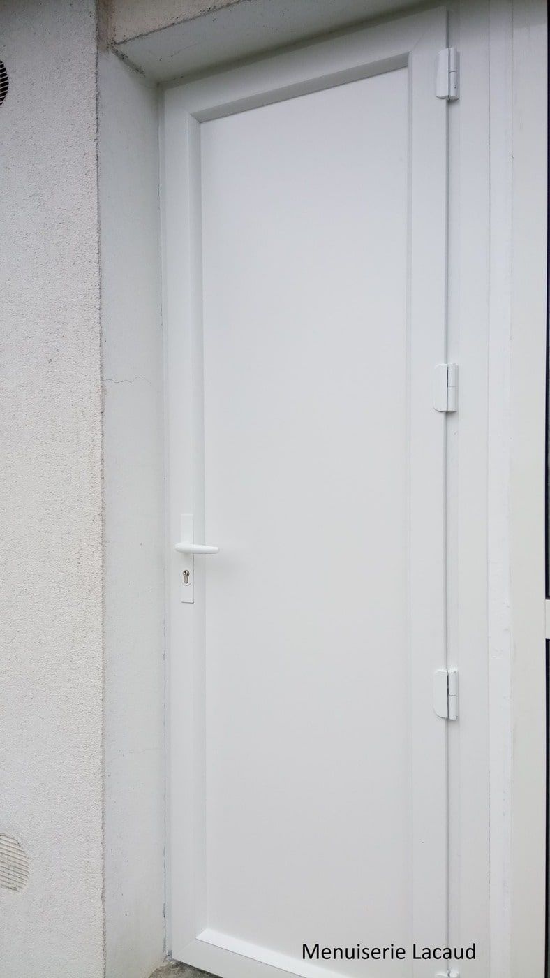 Porte extérieure blanche encastrée dans un mur gris clair, avec une poignée et des charnières simples.