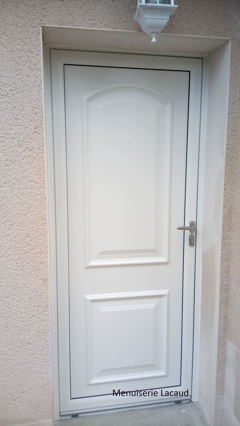 Porte extérieure blanche avec poignée argentée encastrée dans un mur en stuc sous un éclairage de porche