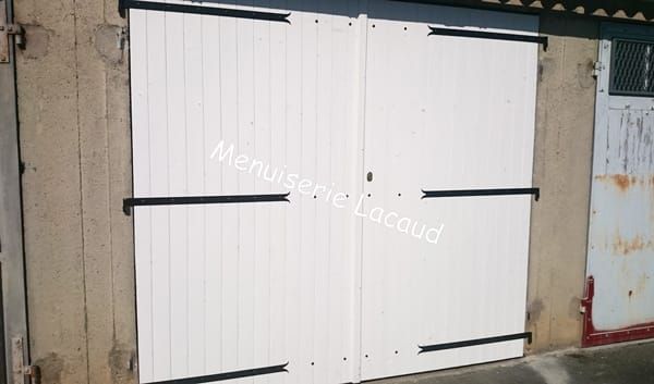 Portes doubles en métal blanc avec charnières noires sur un mur d'immeuble usé