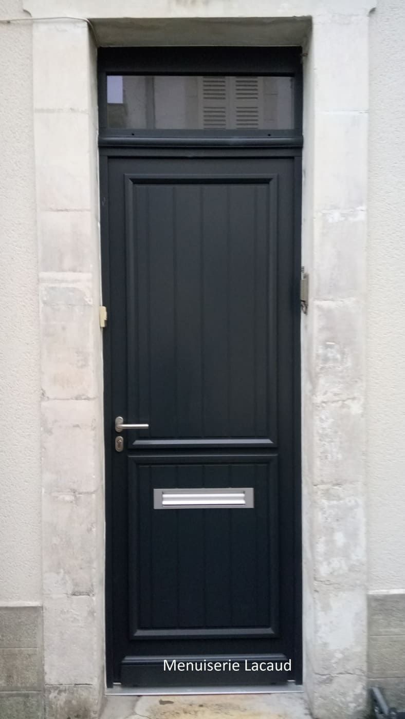 Porte d'entrée noire avec fente à lettres dans un encadrement de porte en pierre