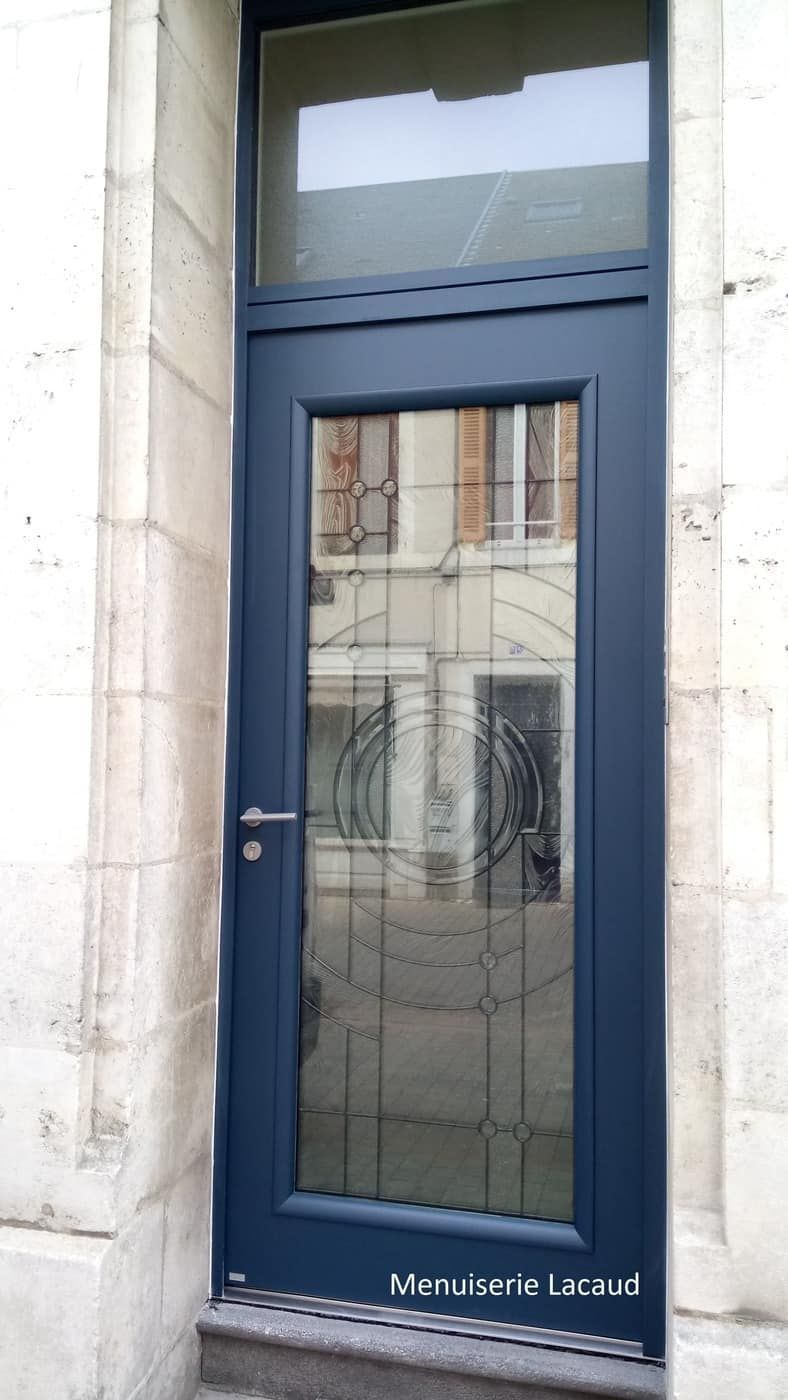 Porte d'entrée étroite à panneaux de verre bleu foncé avec imposte dans une façade d'immeuble en pierre