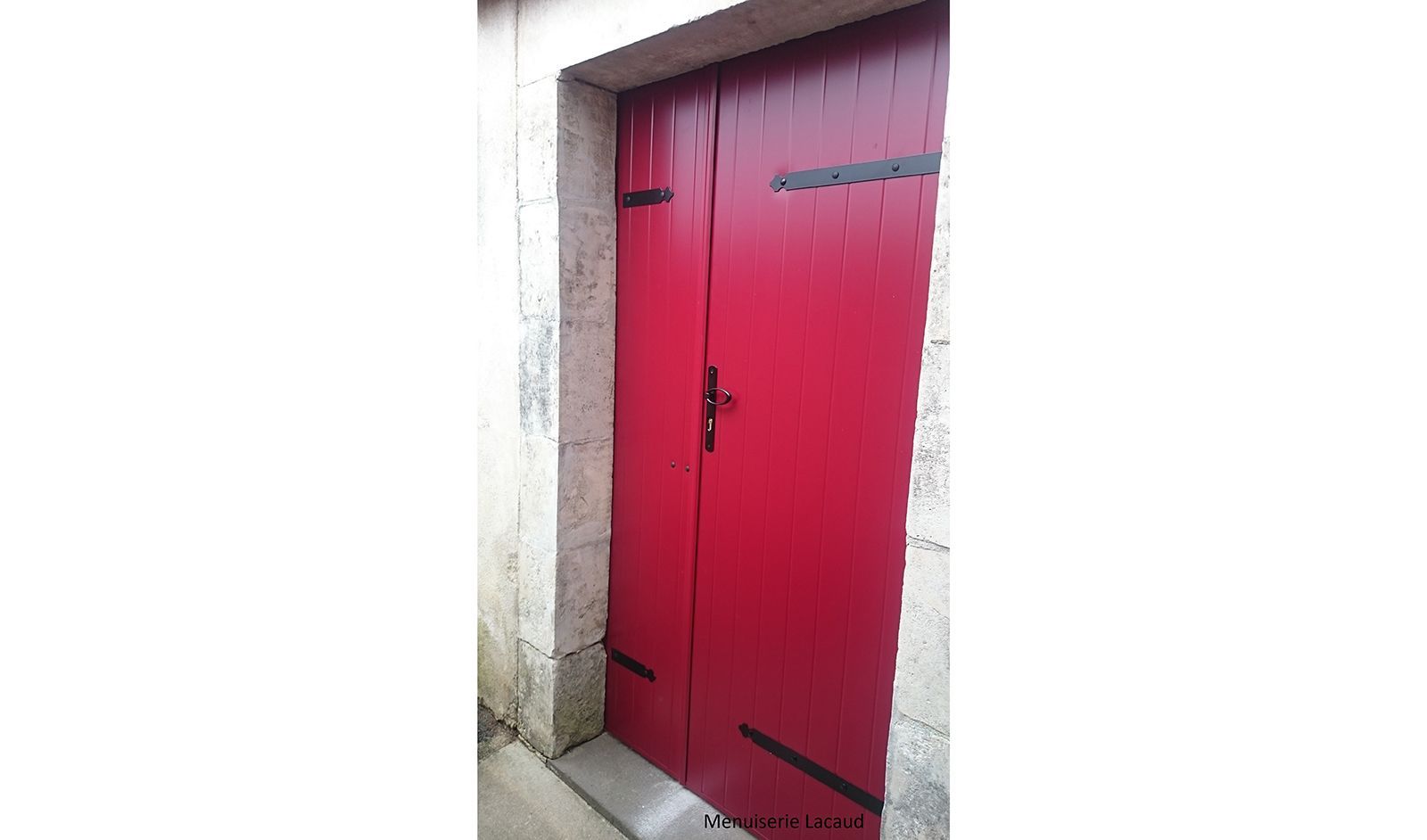 Porte en métal rouge encastrée dans un mur en pierre, avec charnières et loquet noirs.