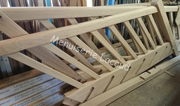 Des fermes en bois empilées dans un atelier, avec des poutres claires et brutes formant des cadres triangulaires.