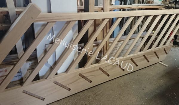Clôture en treillis de bois appuyée contre un mur, avec un support diagonal et des lattes découpées.