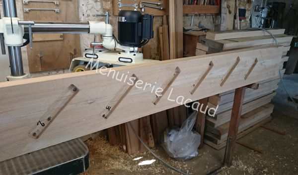 Atelier de menuiserie avec une grande caisse en bois brut en forme de cercueil posée sur des tréteaux, avec des serre-joints et des outils à proximité.
