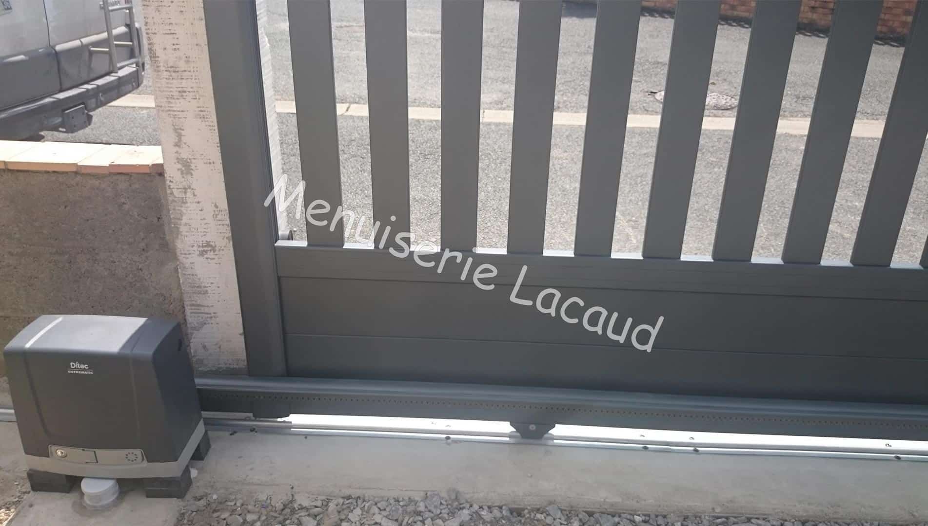 Portail en métal noir avec inscriptions blanches, pilier en pierre et petite boîte sur le côté gauche.