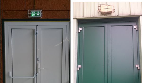 Deux portes doubles grises avec des panneaux de sortie de secours au-dessus, dans un couloir intérieur.
