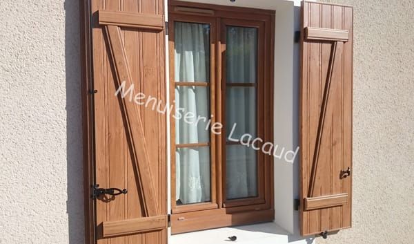 Fenêtre à volets en bois avec cadre marron et rideaux beiges sur un mur extérieur en stuc