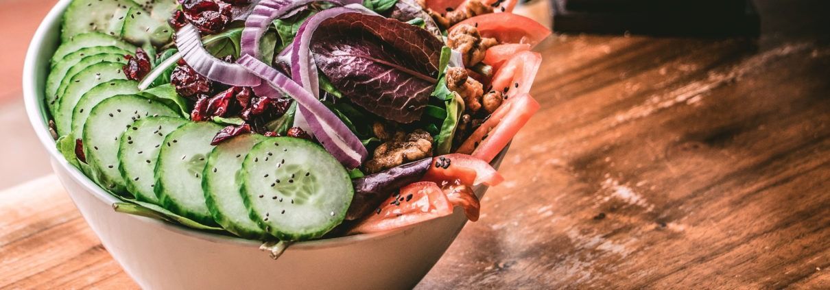 Un tazón de ensalada con pepinos, cebollas y tomates en una mesa de madera.