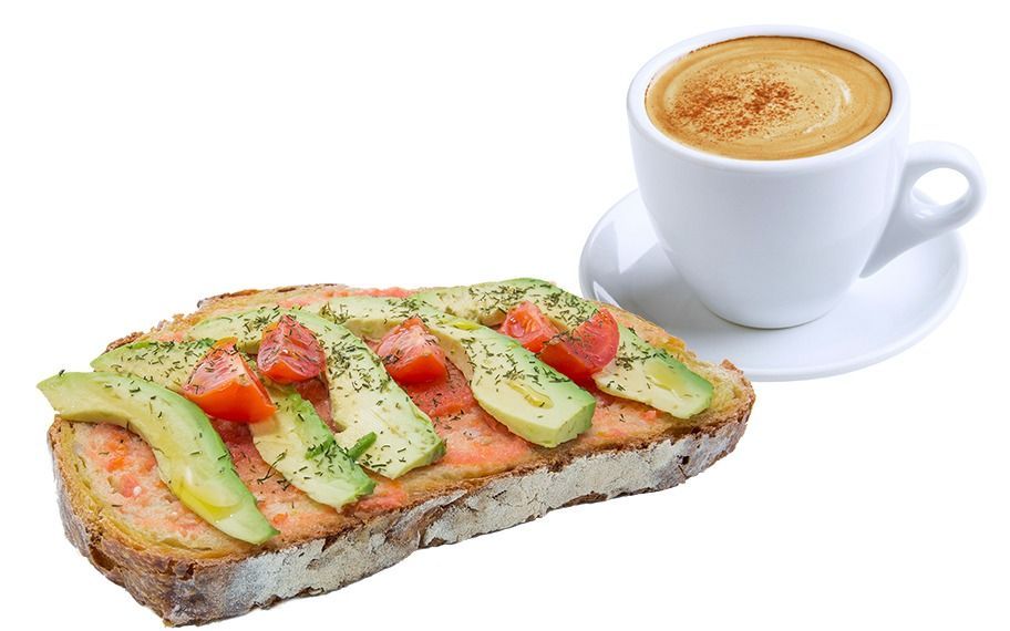 Un sándwich con aguacate y tomate junto a una taza de café.