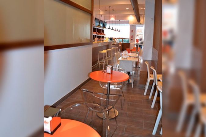 Un restaurante con mesas naranjas y sillas transparentes.