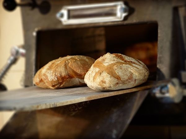 Dos hogazas de pan están colocadas sobre una tabla de cortar de madera delante de un horno.