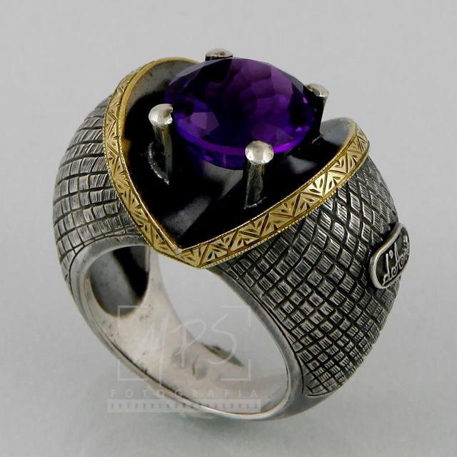 Um anel de prata com uma faixa texturizada em forma de grade, uma borda ornamentada em ouro 