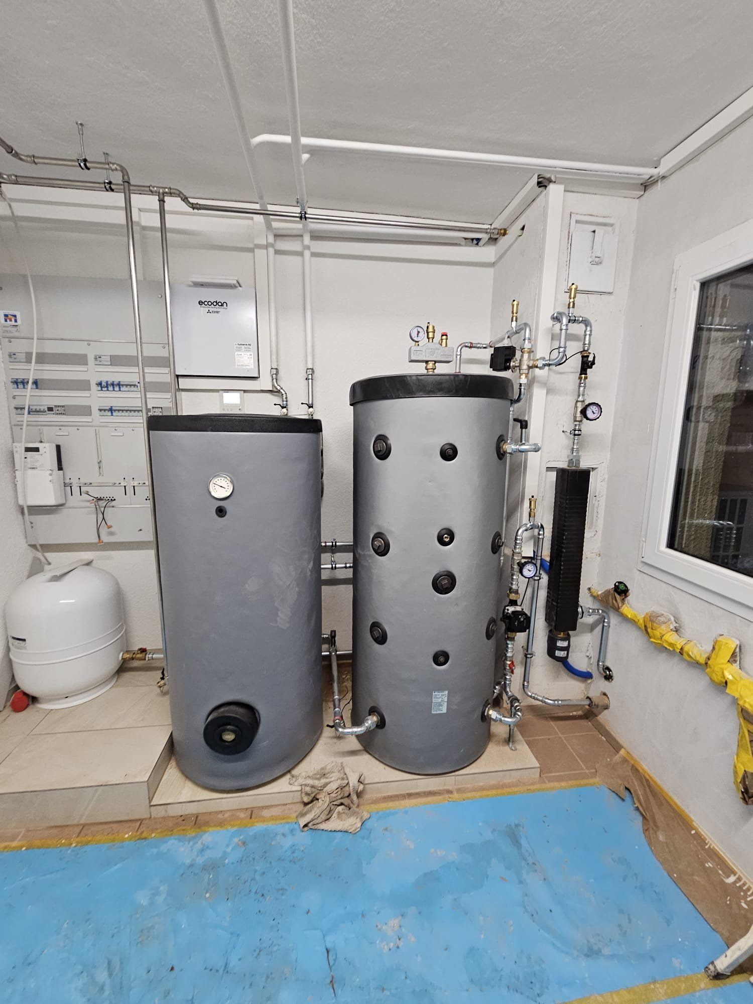 Zwei Grauwassertanks in einem Hauswirtschaftsraum mit Rohren und Messgeräten.