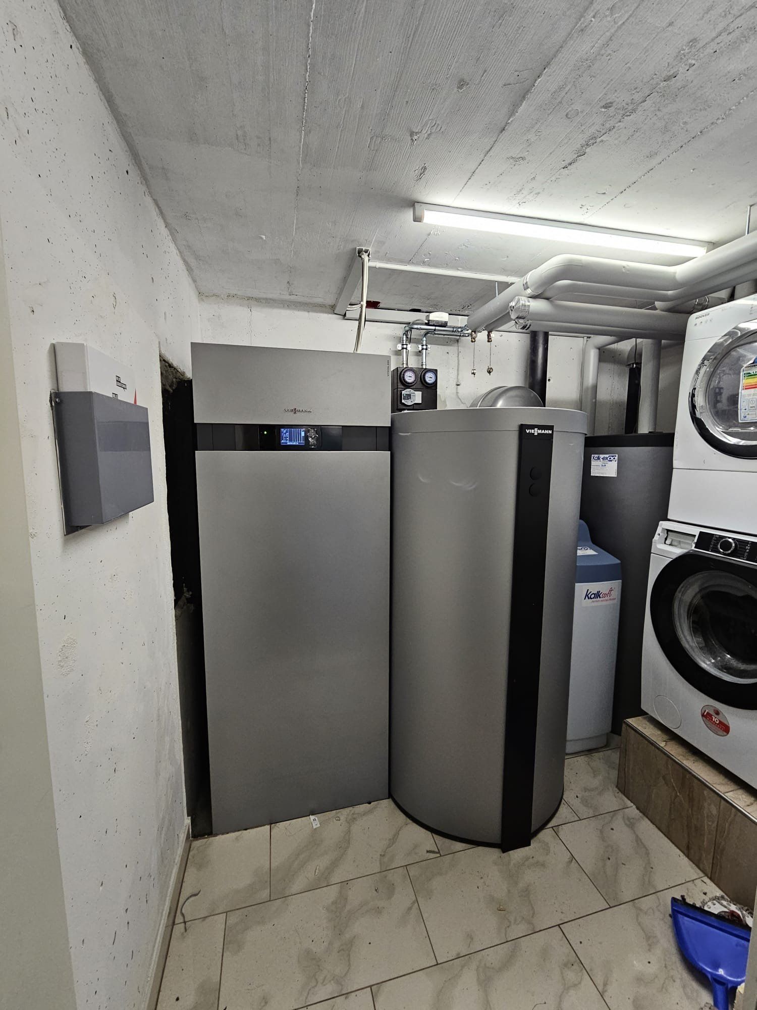 Ein Keller mit Heizungsanlage: ein grosser grauer Heizkessel, Warmwasserbereiter, Waschmaschine, Wasseraufbereitungsanlage.