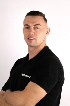 Mann mit kurzen Haaren, schwarzem Poloshirt, verschränkte Arme, lächelnd, vor weissem Hintergrund.