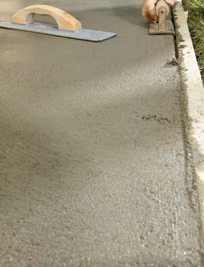 Une personne répand du béton sur un trottoir avec une truelle