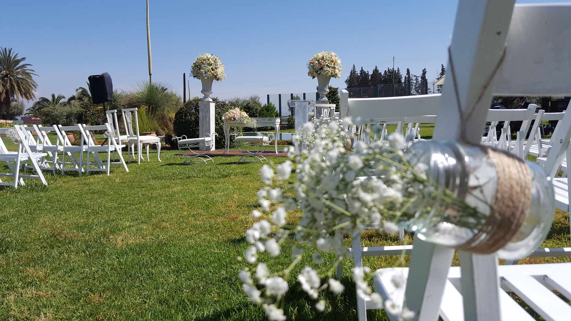 Se está celebrando una ceremonia de boda en un campo con sillas blancas y flores.