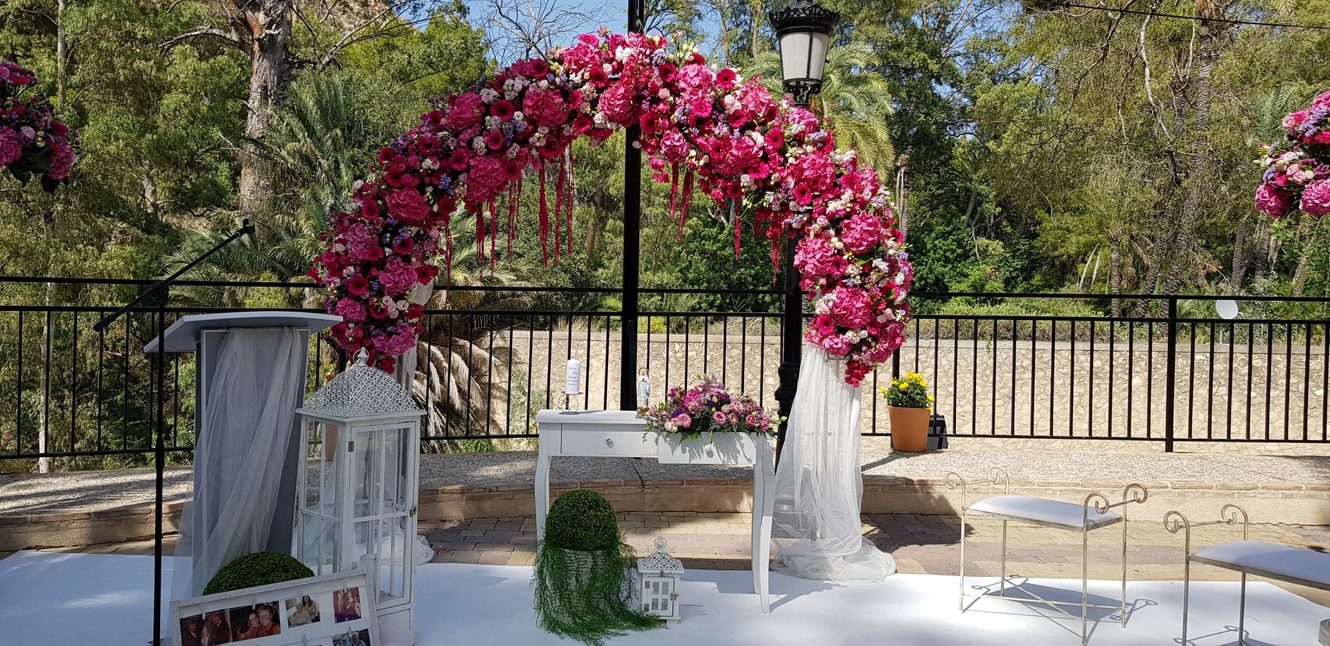 Un arco de boda decorado con flores rosas se encuentra frente a una valla.