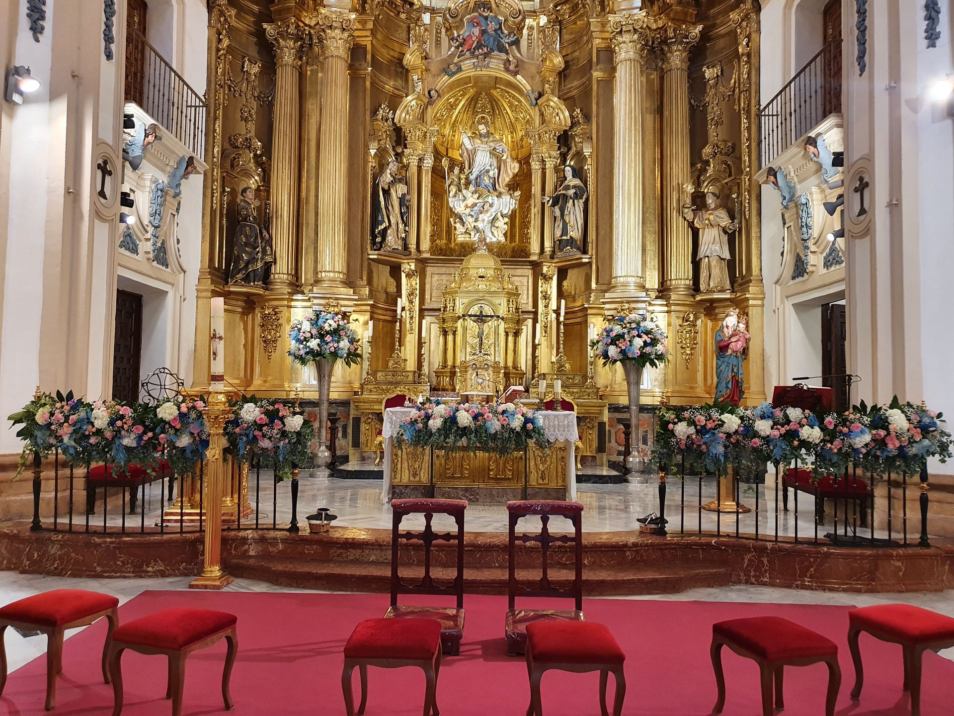 El altar de una iglesia está decorado con flores y taburetes.