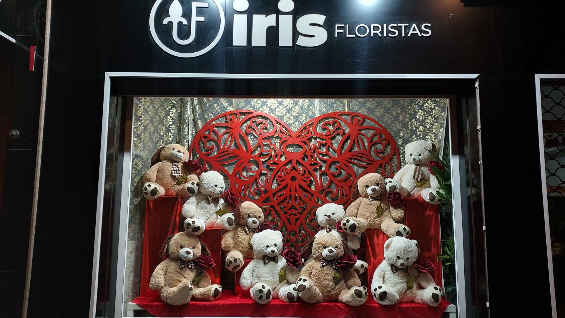 Un grupo de osos de peluche están sentados frente a un corazón en el escaparate de una tienda.