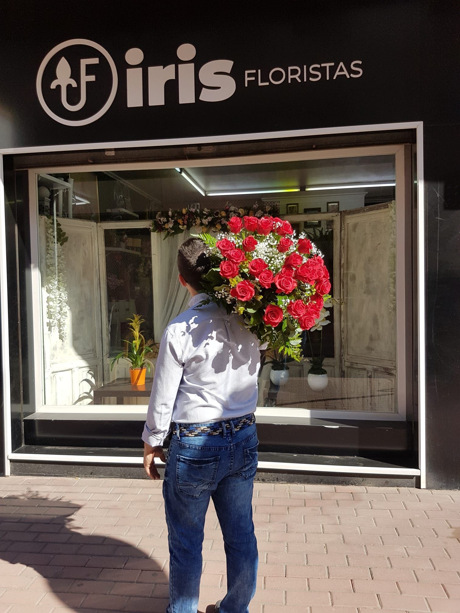 Un hombre lleva un gran ramo de rosas rojas frente a una tienda llamada Iris.