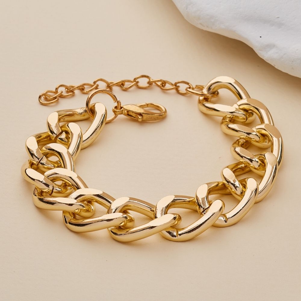 Pulsera de cadena dorada sobre una superficie beige con un pequeño detalle de tela blanca.