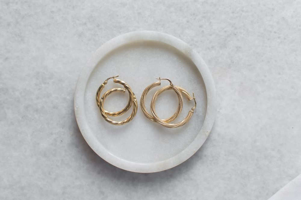 Dos pendientes de aro dorados sobre un pequeño plato blanco.