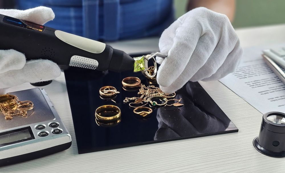 Unas manos enguantadas inspeccionan anillos de oro sobre una bandeja negra junto a una lupa y herramientas.