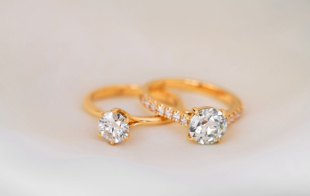 Dos anillos de oro con engastes de diamantes redondos sobre un fondo blanco.