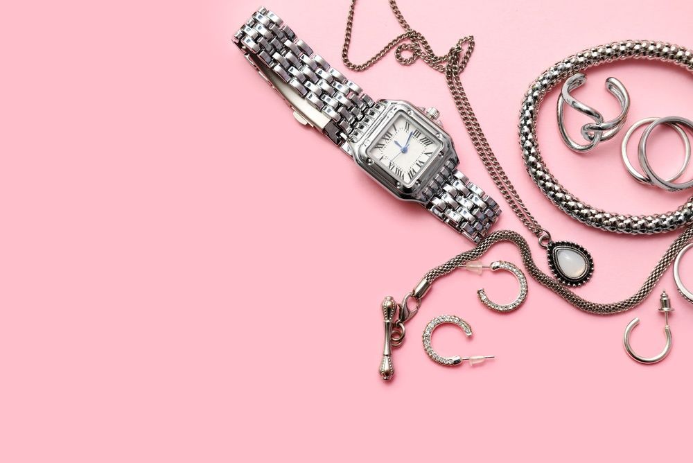 Reloj de pulsera plateado con cadenas y ganchos sobre un fondo rosa.